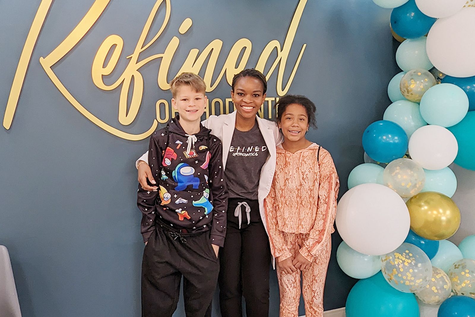 Dr. Bonolo with two young patients at the Refined Orthodontics sign