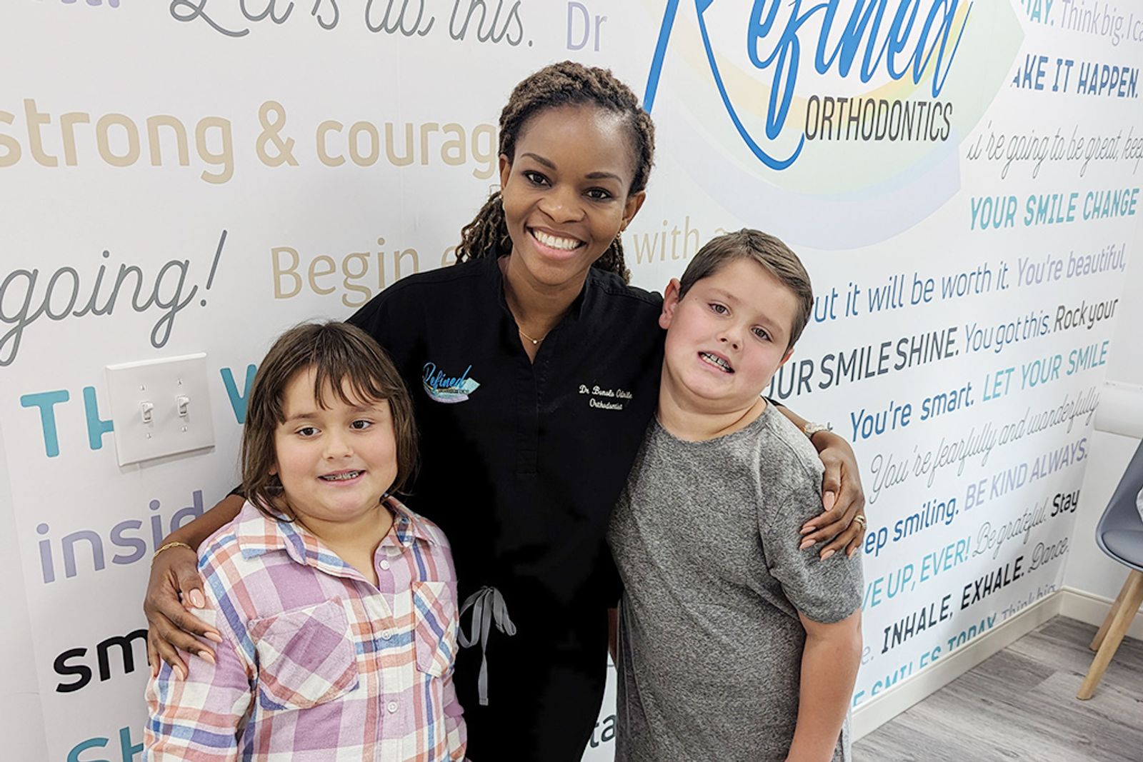 Dr. Bonolo with two young patients at the Refined Orthodontics smile wall