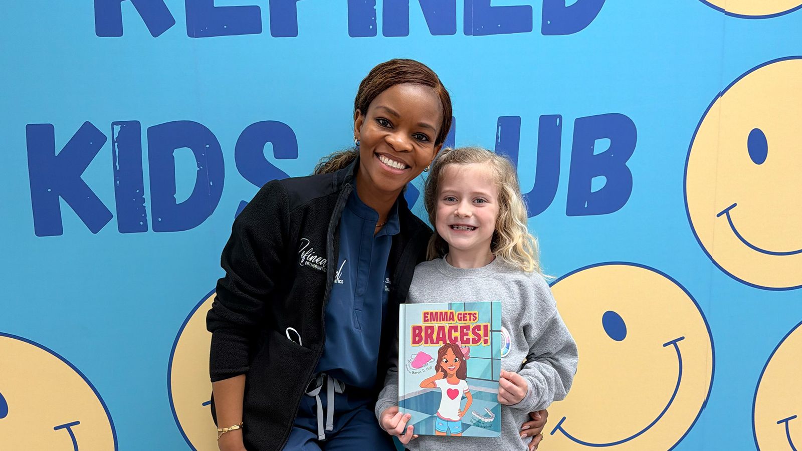 Dr. Bonolo reading Emma Gets Braces with a young patient at the Kids Club wall