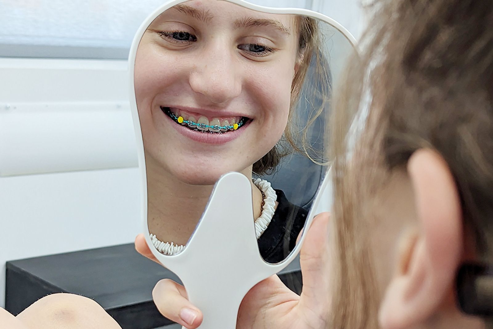 A patient with braces smiling into a hand mirror at Refined Orthodontics