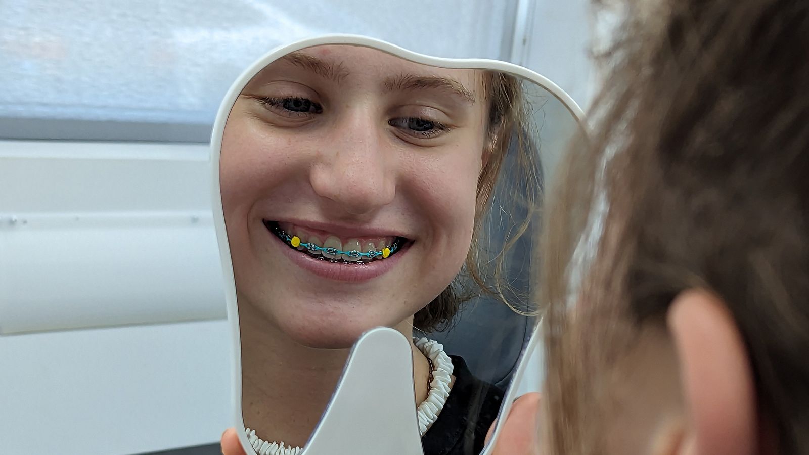 A patient with braces checking her smile in a tooth-shaped mirror at Refined Orthodontics