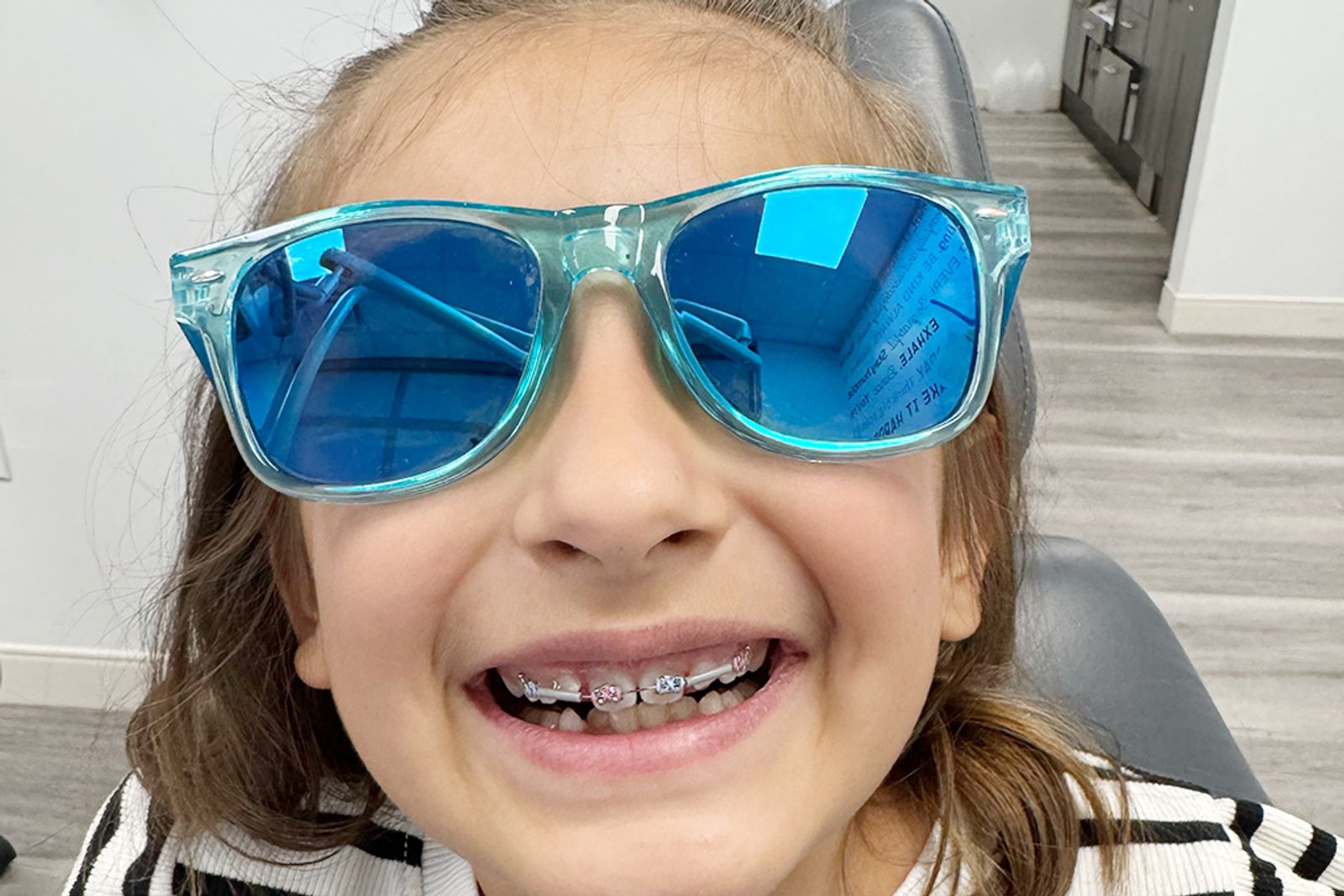 A young patient showing off colored braces and sunglasses